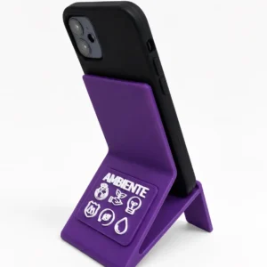 Teléfono celular negro colocado de espaldas sobre un soporte de bioplástico violeta con la inscripción AMBIENTE e íconos ecológicos en blanco, sobre fondo blanco.